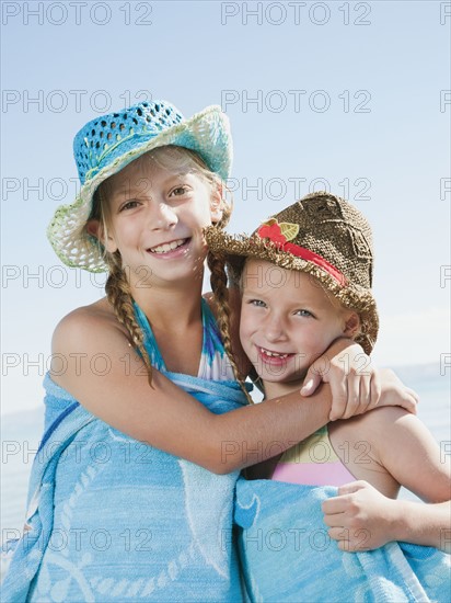 Portrait of girls (6-7,8-9) wrapped in towel on beach.