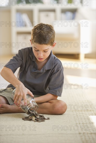 Boy (10-11) sitting on floor and taking out coin from jar. Photo : Daniel Grill