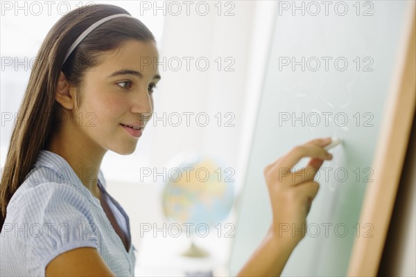 Girl (12-13) writing on chalk board in class.