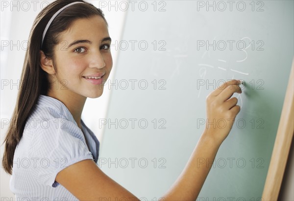 Portrait of girl (12-13) writing on chalk board in class.