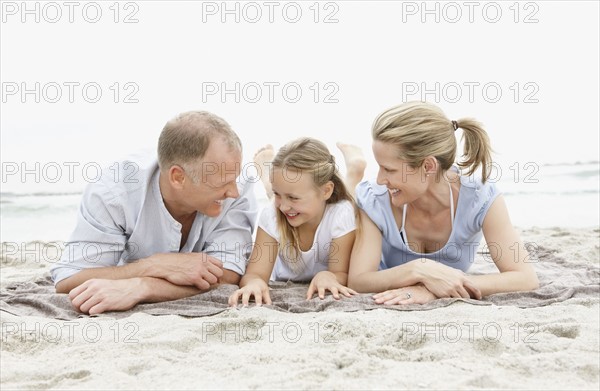 Two parents lying on beach with daughter (10-11). Photo : Momentimages