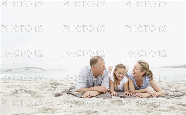 Two parents lying on beach with daughter (10-11). Photo : Momentimages