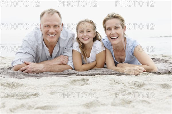 Two parents lying on beach with daughter (10-11). Photo : Momentimages