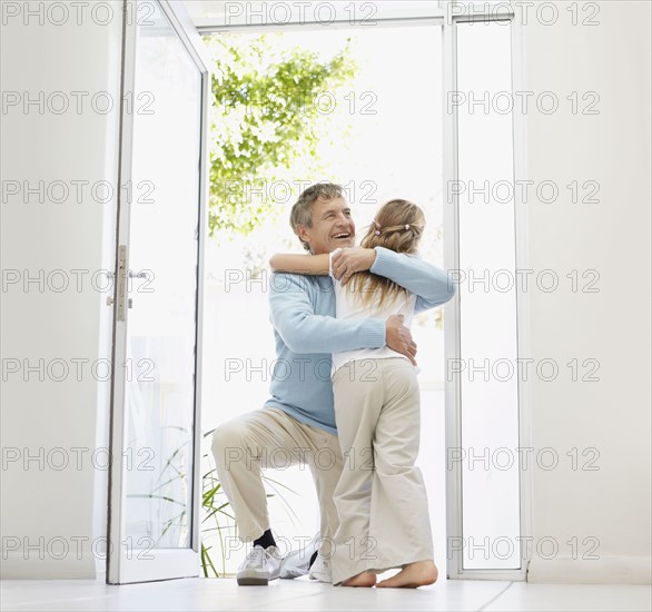 Granddaughter (10-11) and grandfather hugging in doorway. Photo : Momentimages