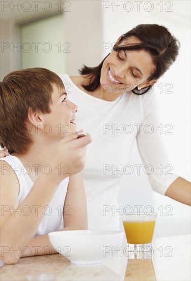 Mother embracing son (12-13) while he is eating breakfast. Photo : Momentimages