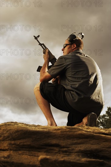 Man holding gun on rocks. Photo : Shawn O'Connor