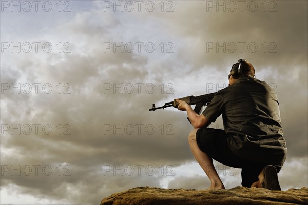 Man aiming gun on rocks. Photo : Shawn O'Connor