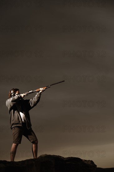 Man aiming rifle on rocks. Photo : Shawn O'Connor