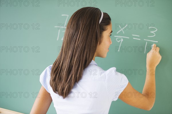 Girl (12-13) writing on chalk board in class.