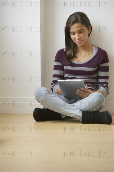 Girl (12-13) using digital tablet on floor.