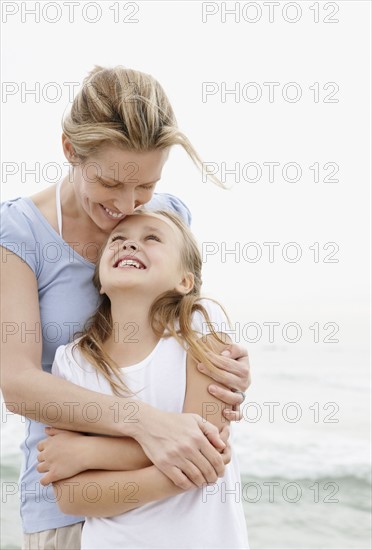 Mother with embracing daughter (10-11) on beach. Photo : Momentimages