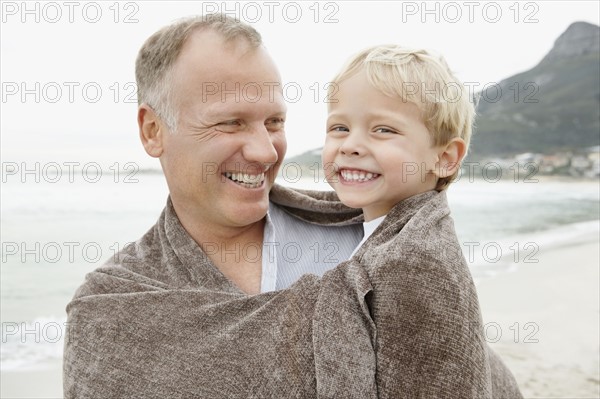 Father carrying son (4-5) on beach. Photo : Momentimages