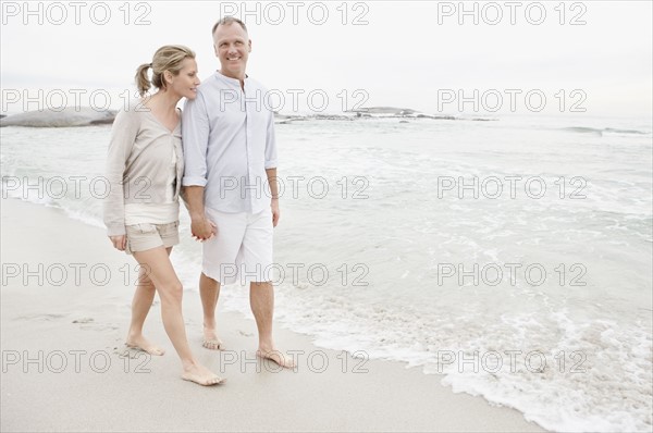 Couple holding hands and walking on empty beach. Photo : Momentimages