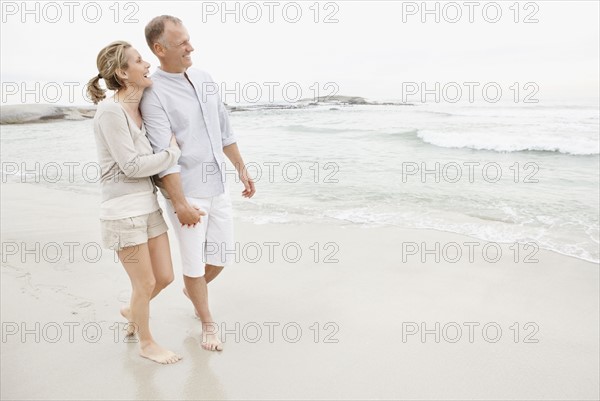 Couple holding hands and walking on empty beach. Photo : Momentimages