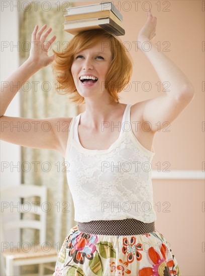 Portrait of young woman balancing books on head. Photo : Jamie Grill