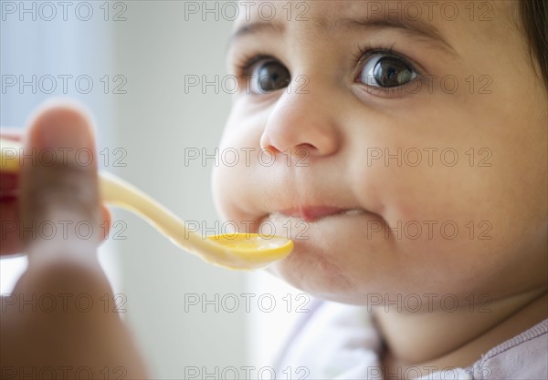 Baby girl (12-18 months) eating from plastic spoon.