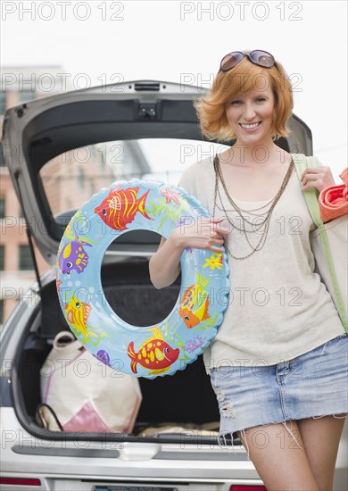 Portrait of young woman with beach gear in front of car. Photo : Jamie Grill