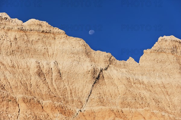 USA, South Dakota, Mountain against blue sky with moon in Badlands National Park.