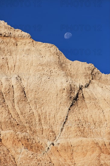 USA, South Dakota, Mountain against blue sky with moon in Badlands National Park.