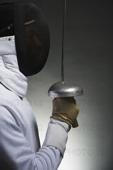 Studio portrait of fencer holding fencing foil.