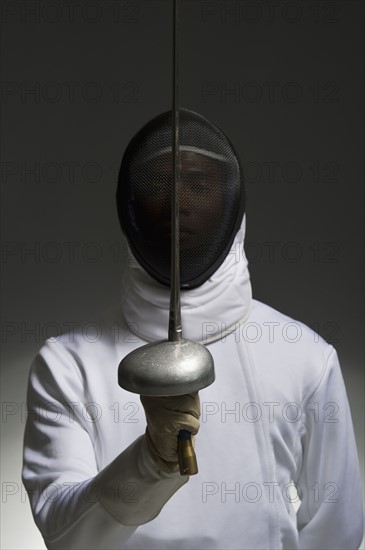 Studio portrait of fencer holding fencing foil.