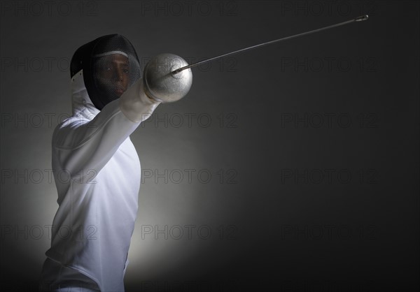 Studio portrait of fencer holding fencing foil.