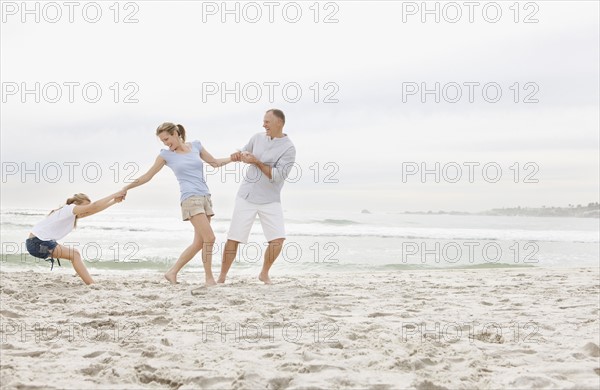 Girl (10-11) playing on beach with parents. Photo : Momentimages