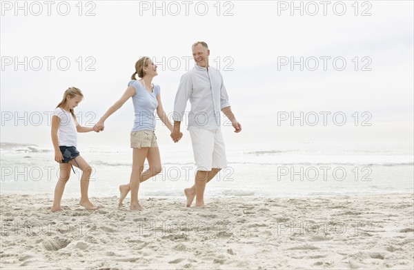 Girl (10-11) walking on beach with parents. Photo : Momentimages