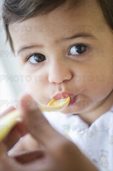 Baby girl (12-18 months) eating from plastic spoon.