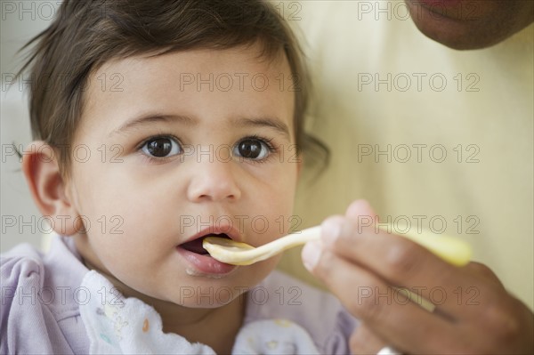 Baby girl (12-18 months) eating from plastic spoon.