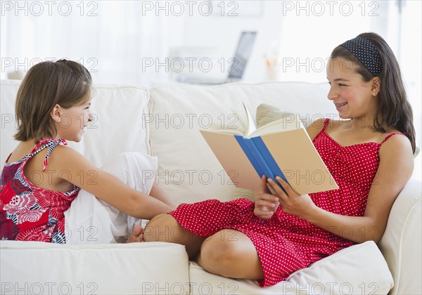 Older sister (12-13) reading book to younger (8-9). Photo : Daniel Grill