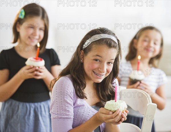 Girls (2-3,8-9,12-13) holding cupcakes with birthday candles. Photo : Daniel Grill