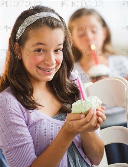 Girls (2-3,12-13) holding cupcakes with birthday candles. Photo : Daniel Grill