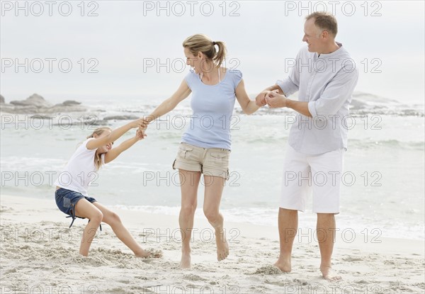 Girl (10-11) playing on beach with parents. Photo : Momentimages