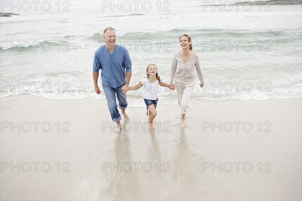 Smiling family holding hands and walking on beach. Photo : Momentimages