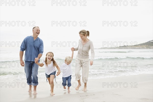 Smiling family holding hands and walking on beach. Photo : Momentimages