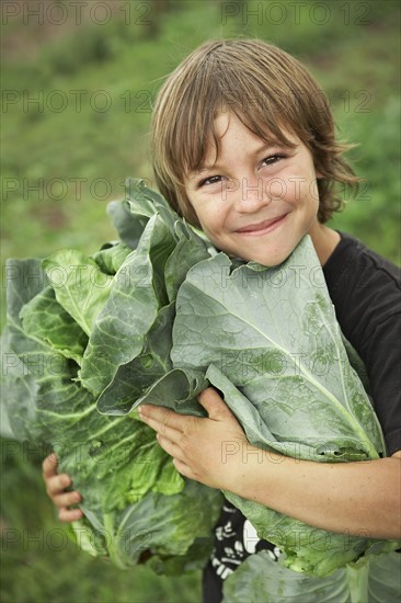 Portrait of boy (6-7) holding lettuces. Photo : Shawn O'Connor