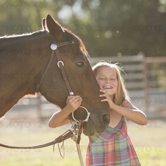 Portrait of smiling cowgirl (8-9) with horse in ranch. Photo : Mike Kemp