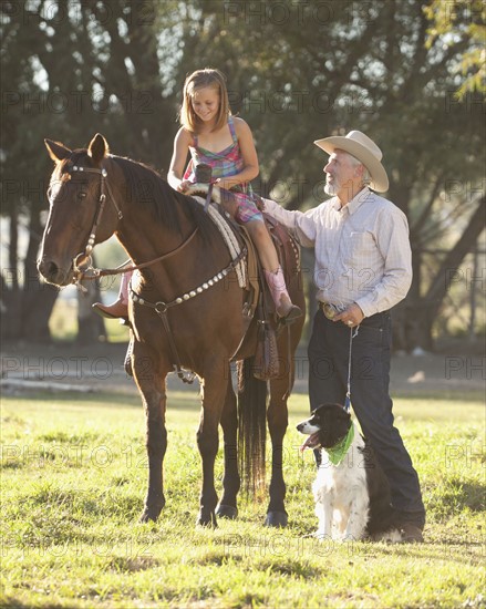 Senior man with dog assisting granddaughter (8-9) horseback riding in ranch. Photo : Mike Kemp