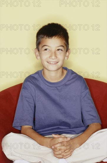 Cute young boy sitting in red chair. Photo : Fisher Litwin