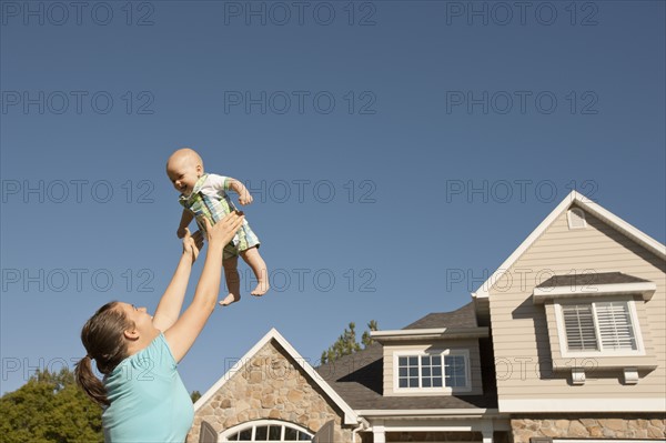 Mother lifting baby boy (6-11 months) outside home. Photo : FBP