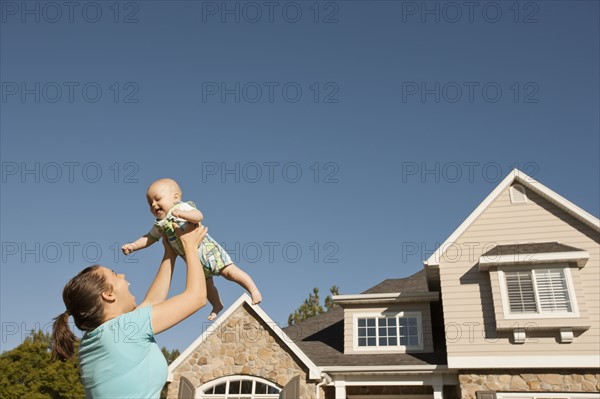 Mother lifting baby boy (6-11 months) outside home. Photo : FBP