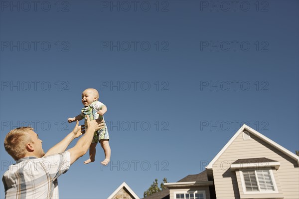 Father lifting baby boy (6-11 months) outside home. Photo : FBP