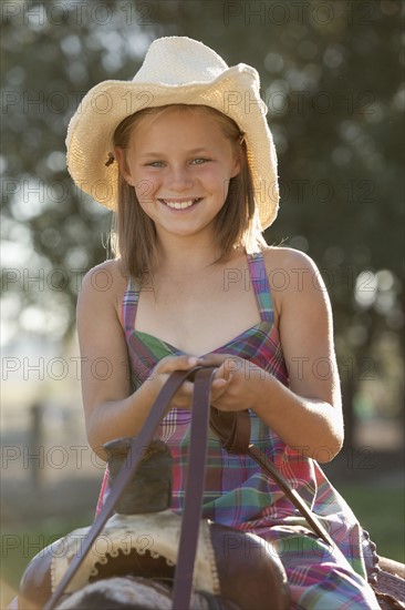 Portrait of smiling cowgirl (8-9) horseback riding in ranch. Photo : Mike Kemp