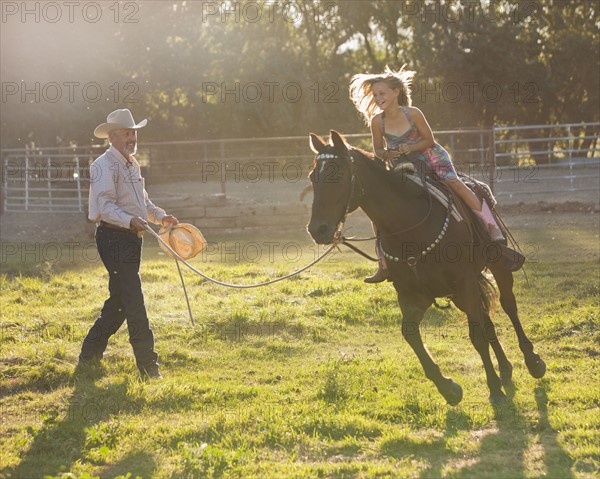 Trainer assisting girl (8-9) riding horse in paddock. Photo : Mike Kemp