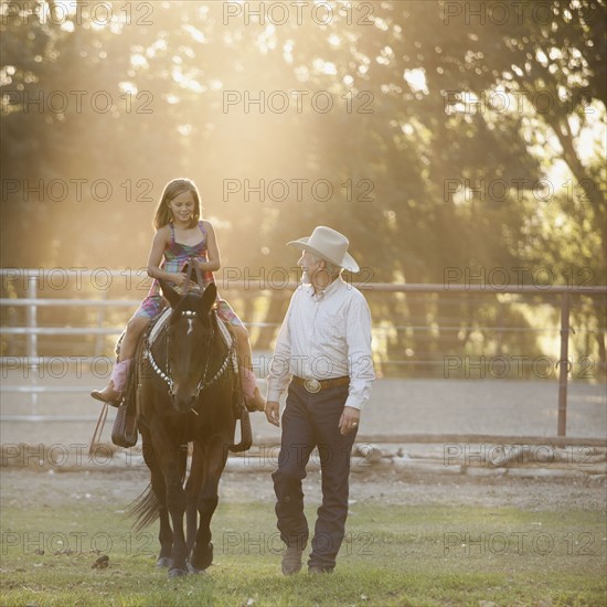 Trainer assisting girl (8-9) riding horse in paddock. Photo : Mike Kemp