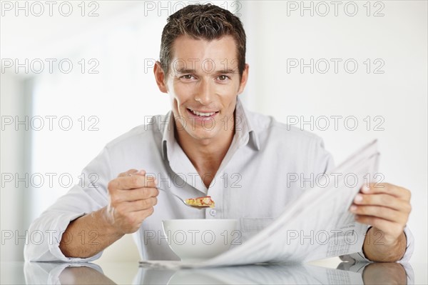 Cheerful mid adult man eating cornflakes and reading newspaper. Photo : Momentimages