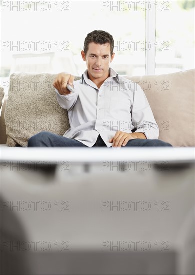 Mid adult man in front of televisionchanging channels. Photo : Momentimages