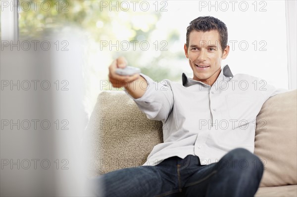 Mid adult man in front of televisionchanging channels. Photo : Momentimages