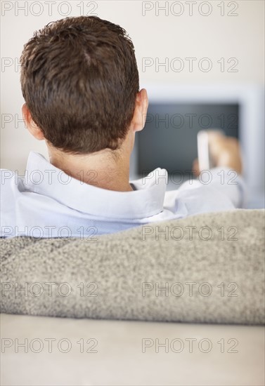 Mid adult man in front of televisionchanging channels. Photo : Momentimages